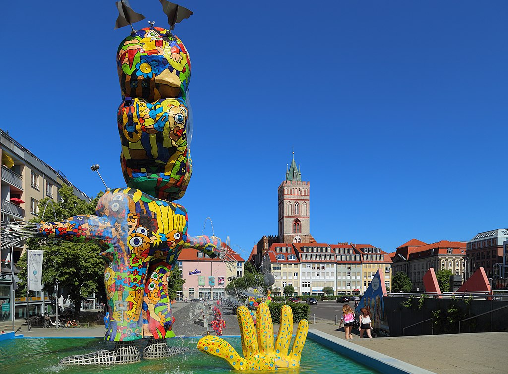 Bunte Statue im Stadtzentrum mit historischer Kirche.